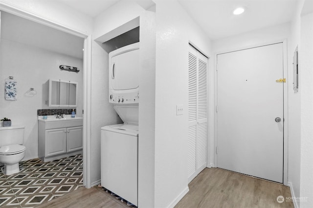 laundry room featuring stacked washer / drying machine, sink, and light hardwood / wood-style floors