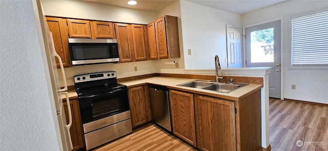 kitchen featuring stainless steel appliances, sink, light wood-type flooring, and kitchen peninsula