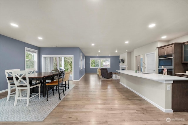 kitchen featuring dark brown cabinetry, sink, an island with sink, double oven, and light hardwood / wood-style floors