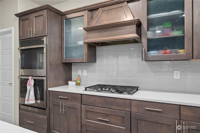 kitchen featuring stainless steel appliances, premium range hood, dark brown cabinets, and tasteful backsplash