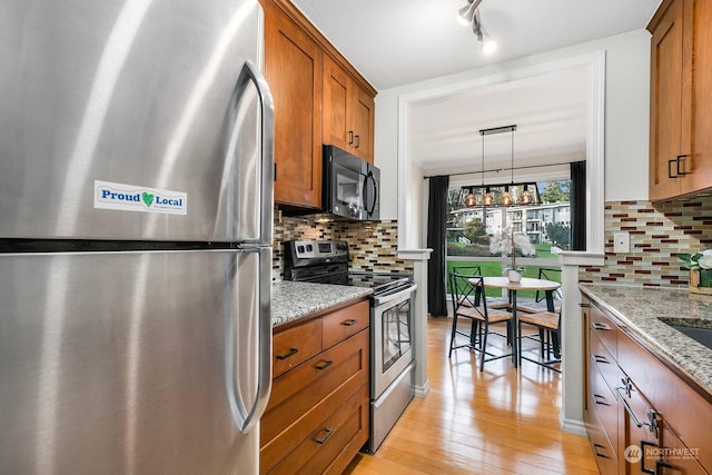 kitchen with light stone counters, tasteful backsplash, pendant lighting, and appliances with stainless steel finishes