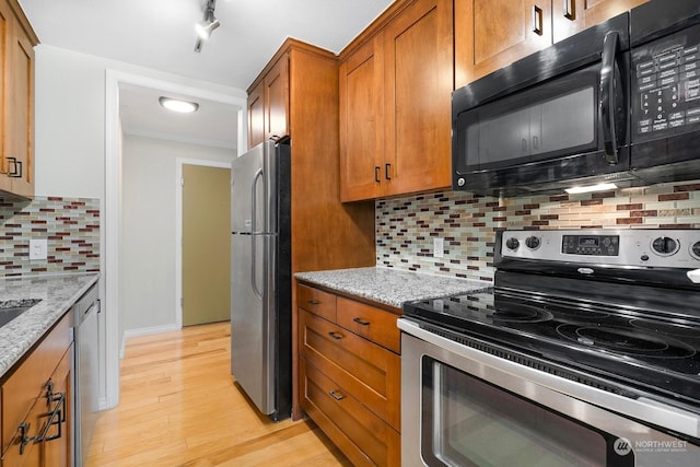 kitchen featuring appliances with stainless steel finishes, tasteful backsplash, track lighting, light stone counters, and light hardwood / wood-style floors