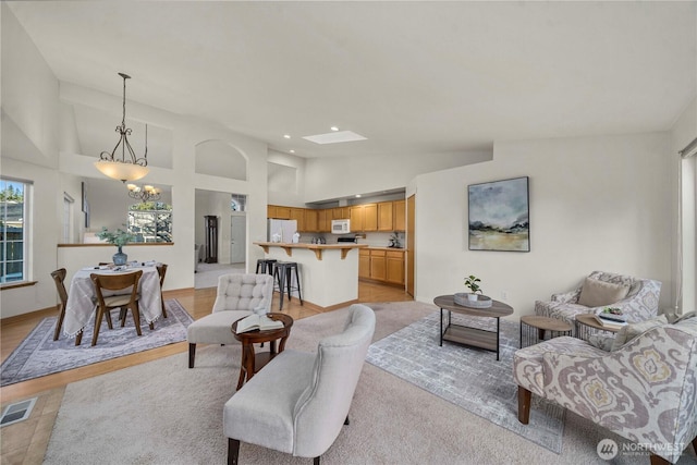 living room with high vaulted ceiling, a skylight, light wood-type flooring, and a notable chandelier