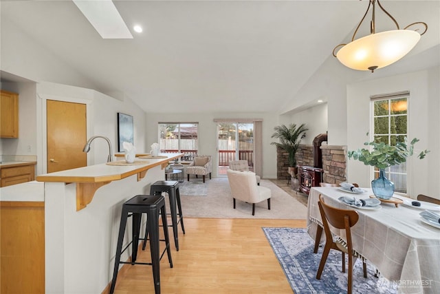 dining space featuring sink, light hardwood / wood-style floors, vaulted ceiling with skylight, and a wood stove