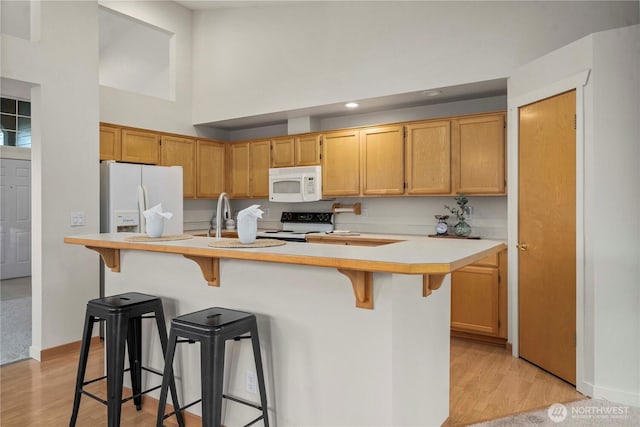 kitchen with a breakfast bar area, a center island with sink, light wood-type flooring, white appliances, and a high ceiling