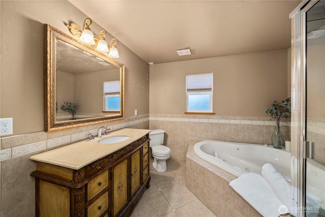 bathroom with tile walls, vanity, a relaxing tiled tub, toilet, and tile patterned floors