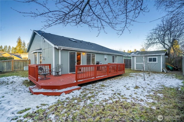 snow covered rear of property with a storage shed and a deck