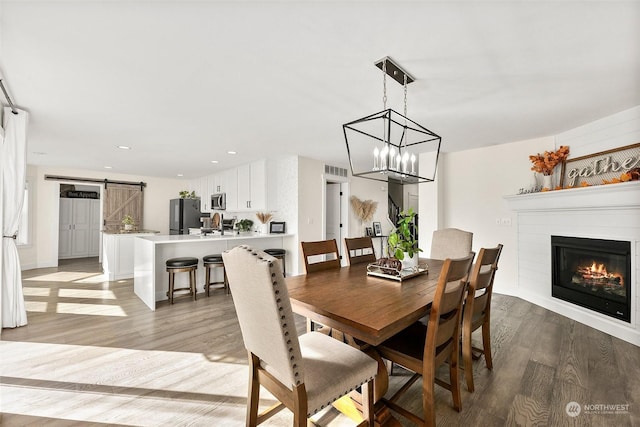 dining area with a notable chandelier, a barn door, and light wood-type flooring