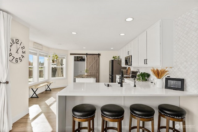 kitchen with appliances with stainless steel finishes, kitchen peninsula, a barn door, light hardwood / wood-style floors, and white cabinets