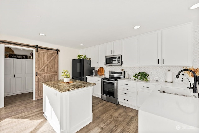 kitchen with sink, appliances with stainless steel finishes, tasteful backsplash, a kitchen island, and a barn door