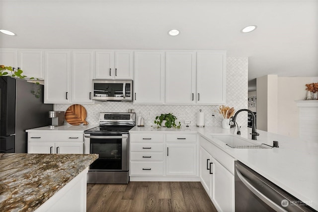 kitchen with appliances with stainless steel finishes, sink, white cabinets, backsplash, and dark wood-type flooring