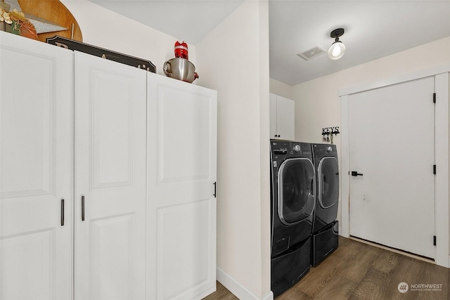 clothes washing area with cabinets, washing machine and clothes dryer, and dark hardwood / wood-style floors