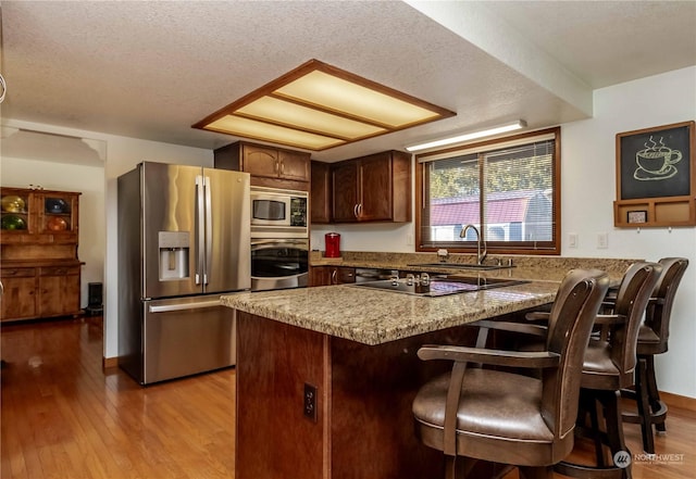 kitchen with sink, a breakfast bar area, light wood-type flooring, stainless steel appliances, and a textured ceiling