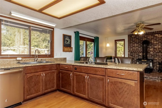 kitchen featuring sink, a wood stove, stainless steel dishwasher, kitchen peninsula, and light hardwood / wood-style flooring