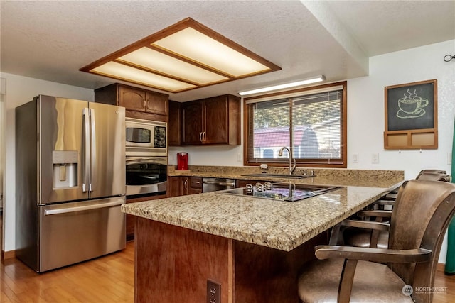 kitchen with sink, light wood-type flooring, appliances with stainless steel finishes, kitchen peninsula, and light stone countertops