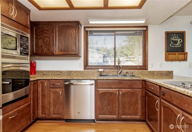 kitchen with sink, stainless steel appliances, light hardwood / wood-style floors, and light stone countertops