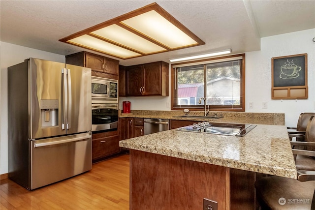 kitchen with sink, stainless steel appliances, a kitchen bar, kitchen peninsula, and light wood-type flooring