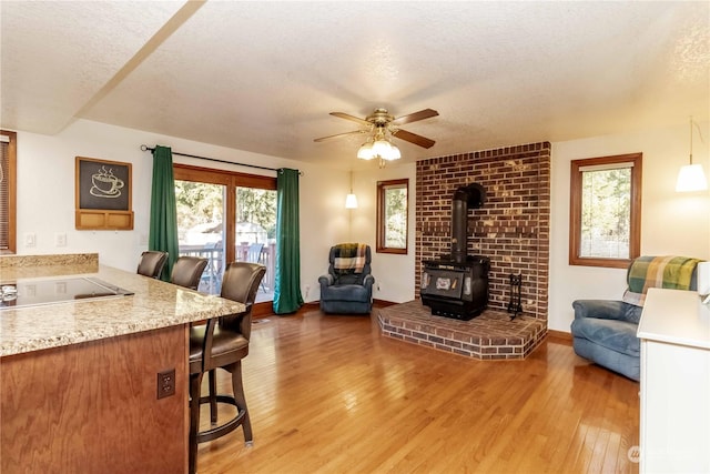 interior space with ceiling fan, a wood stove, a textured ceiling, and light wood-type flooring