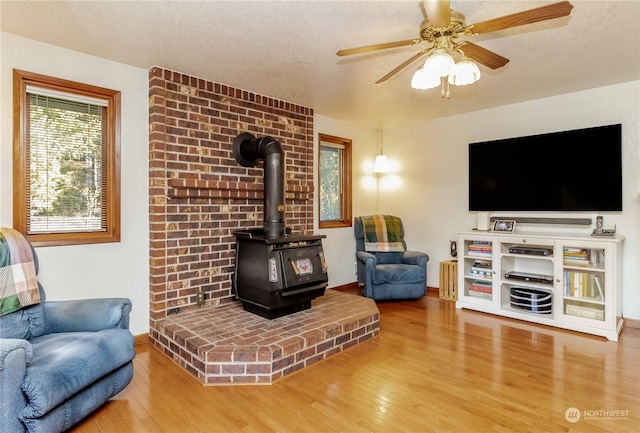 living room with hardwood / wood-style flooring, a textured ceiling, ceiling fan, and a wood stove