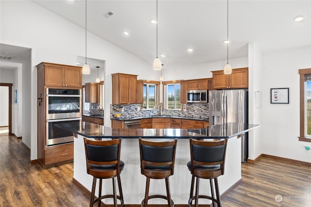 kitchen featuring sink, appliances with stainless steel finishes, a center island, tasteful backsplash, and decorative light fixtures