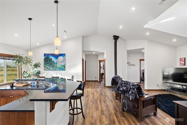 kitchen featuring a breakfast bar, vaulted ceiling, dark hardwood / wood-style floors, pendant lighting, and dark stone counters