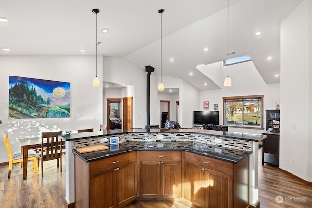 kitchen featuring decorative backsplash, dark hardwood / wood-style flooring, decorative light fixtures, vaulted ceiling, and dark stone counters