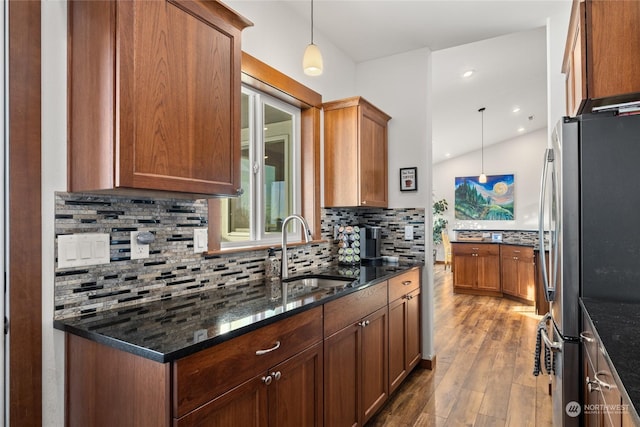 kitchen with sink, hanging light fixtures, dark stone countertops, stainless steel refrigerator, and hardwood / wood-style floors