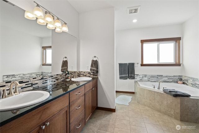 bathroom featuring a relaxing tiled tub, plenty of natural light, tile patterned flooring, and vanity