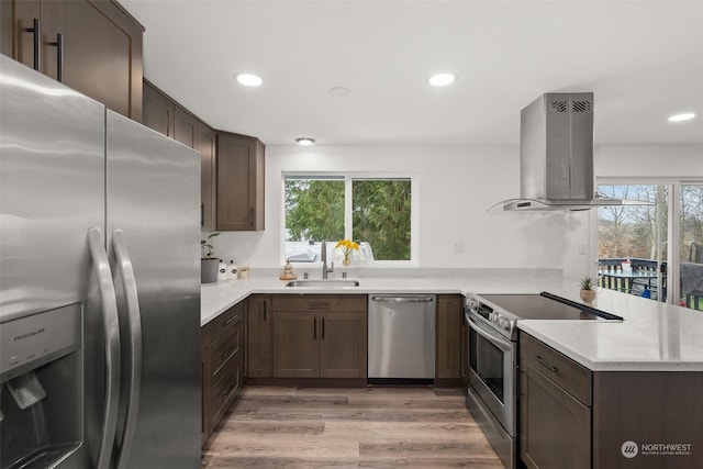 kitchen featuring sink, island range hood, kitchen peninsula, stainless steel appliances, and light hardwood / wood-style floors