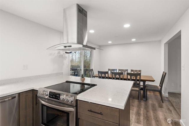 kitchen featuring hardwood / wood-style flooring, dark brown cabinets, stainless steel appliances, island exhaust hood, and kitchen peninsula