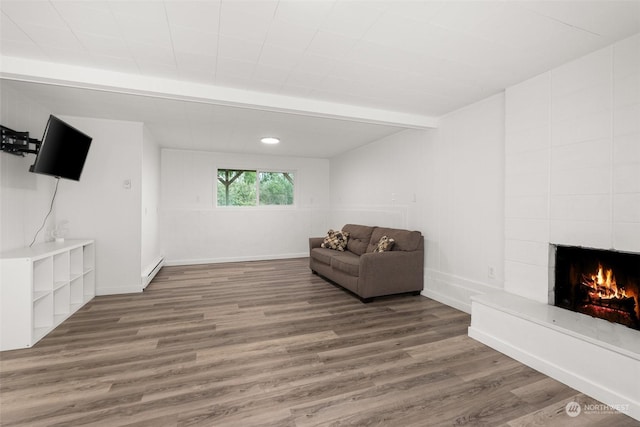 living area with beamed ceiling, a baseboard heating unit, hardwood / wood-style floors, and a fireplace