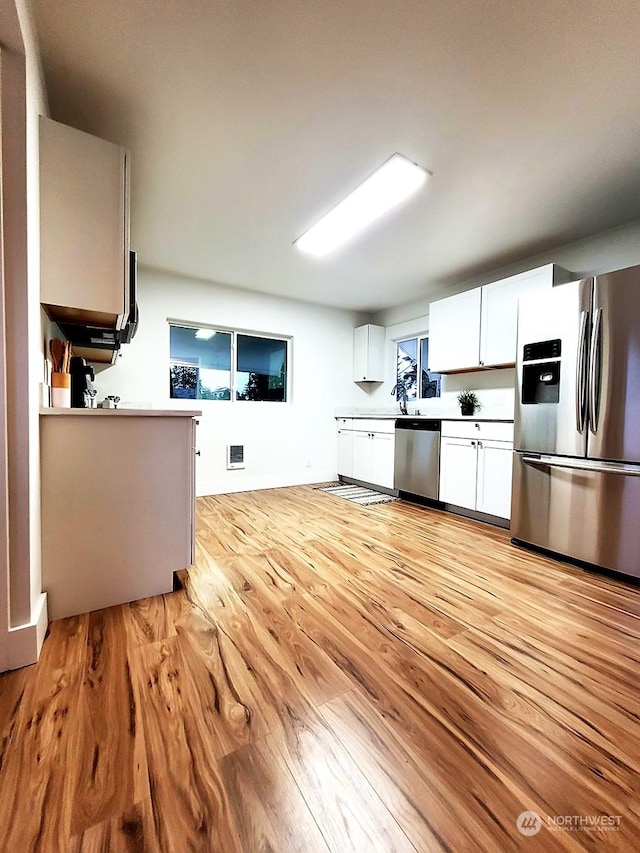 kitchen with light wood-type flooring, white cabinets, and appliances with stainless steel finishes