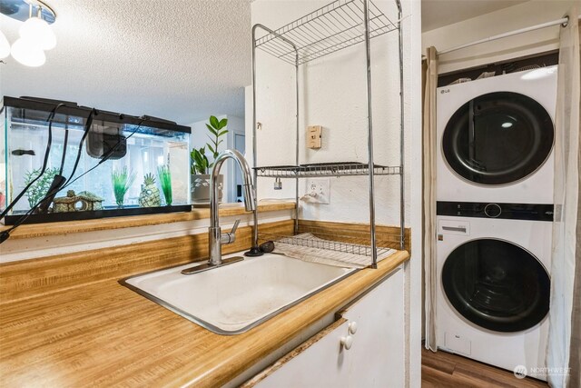 clothes washing area with stacked washer and dryer, dark hardwood / wood-style floors, sink, and a textured ceiling