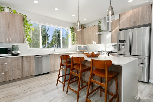 kitchen featuring a kitchen island, appliances with stainless steel finishes, a breakfast bar, hanging light fixtures, and wall chimney exhaust hood