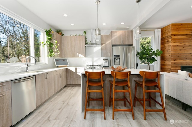 kitchen featuring wall chimney exhaust hood, light brown cabinetry, a breakfast bar area, pendant lighting, and stainless steel appliances