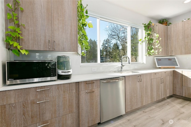 kitchen with stainless steel appliances, sink, light brown cabinetry, and light hardwood / wood-style flooring