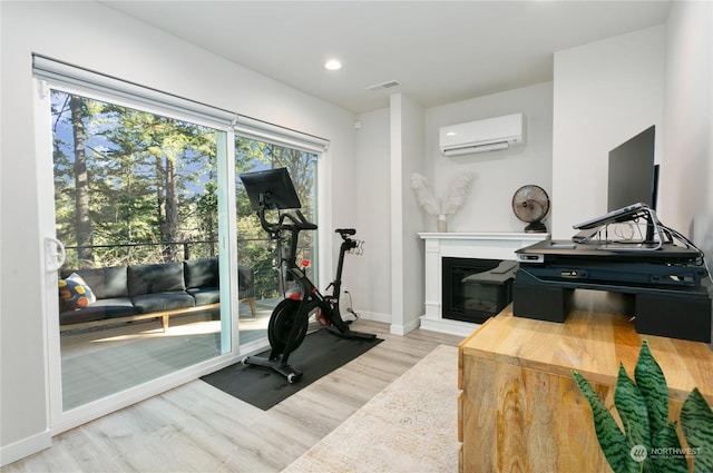 exercise area with a wall unit AC and light hardwood / wood-style flooring