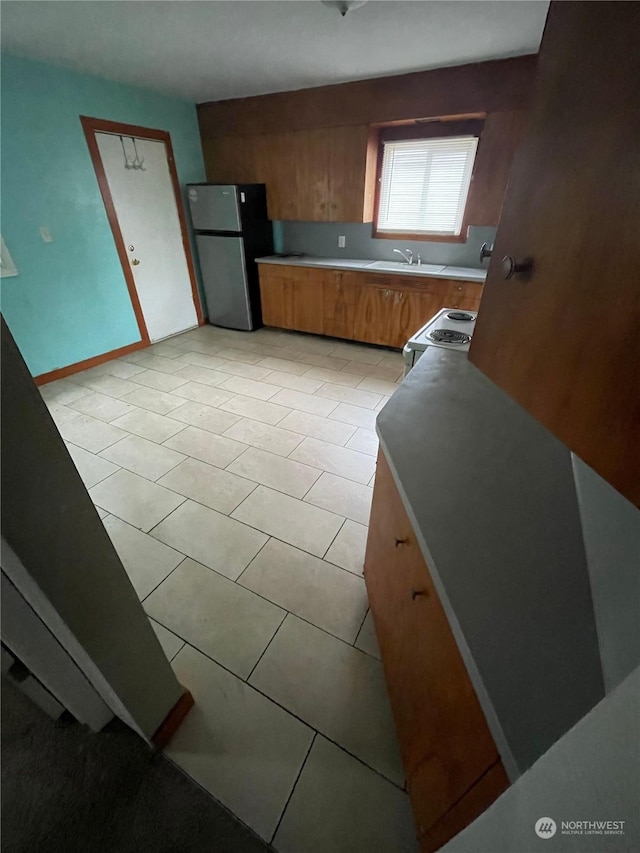 kitchen with sink, light tile patterned floors, stainless steel refrigerator, and electric stove