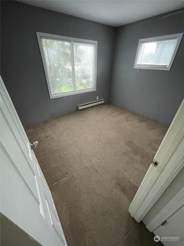 unfurnished room featuring a baseboard heating unit and carpet flooring