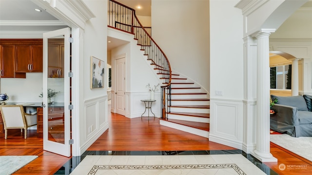 stairway with ornate columns, wood-type flooring, and crown molding