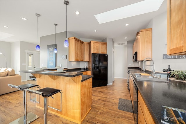 kitchen with a kitchen bar, light hardwood / wood-style flooring, kitchen peninsula, pendant lighting, and black appliances