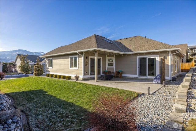 back of house with a patio, a yard, roof with shingles, and a mountain view