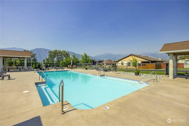 community pool with a patio area, fence, and a mountain view