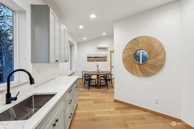 kitchen featuring sink, gray cabinetry, light stone counters, vaulted ceiling, and light wood-type flooring