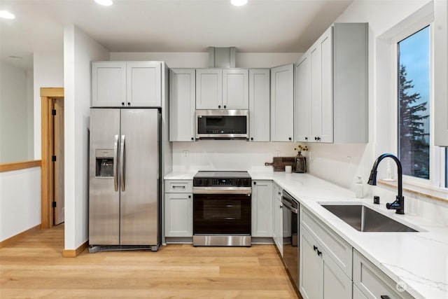 kitchen with sink, light hardwood / wood-style floors, light stone countertops, and appliances with stainless steel finishes