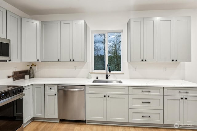 kitchen featuring light stone counters, appliances with stainless steel finishes, light hardwood / wood-style floors, and sink