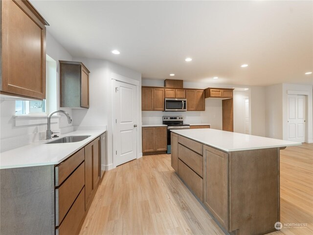 kitchen with appliances with stainless steel finishes, light hardwood / wood-style floors, sink, and a kitchen island