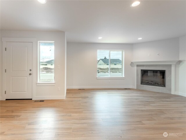 unfurnished living room with a tiled fireplace and light hardwood / wood-style floors