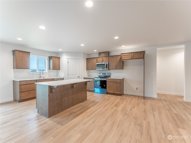 kitchen featuring sink, a kitchen bar, a center island, stainless steel appliances, and light hardwood / wood-style flooring