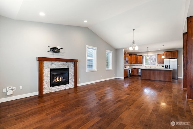 unfurnished living room featuring vaulted ceiling, a stone fireplace, sink, a chandelier, and dark wood-type flooring